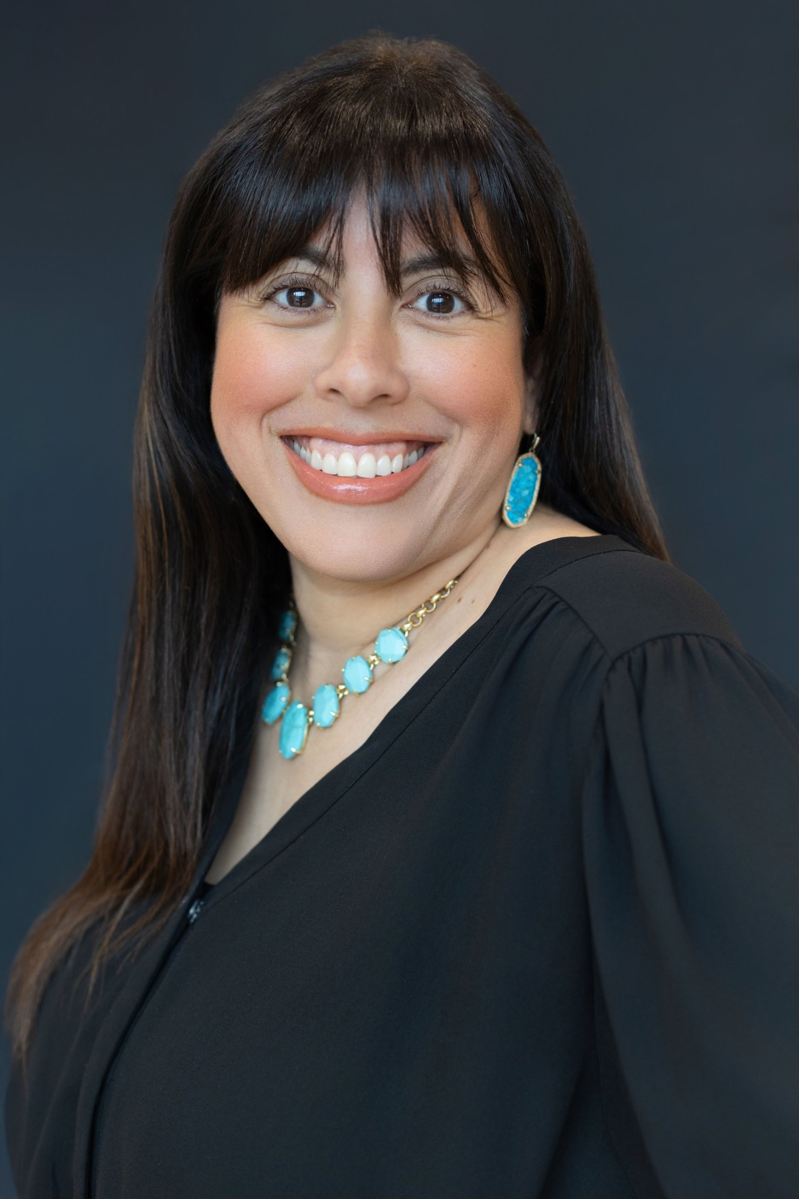 Holly Subervi headshot in a black top and turquoise necklace