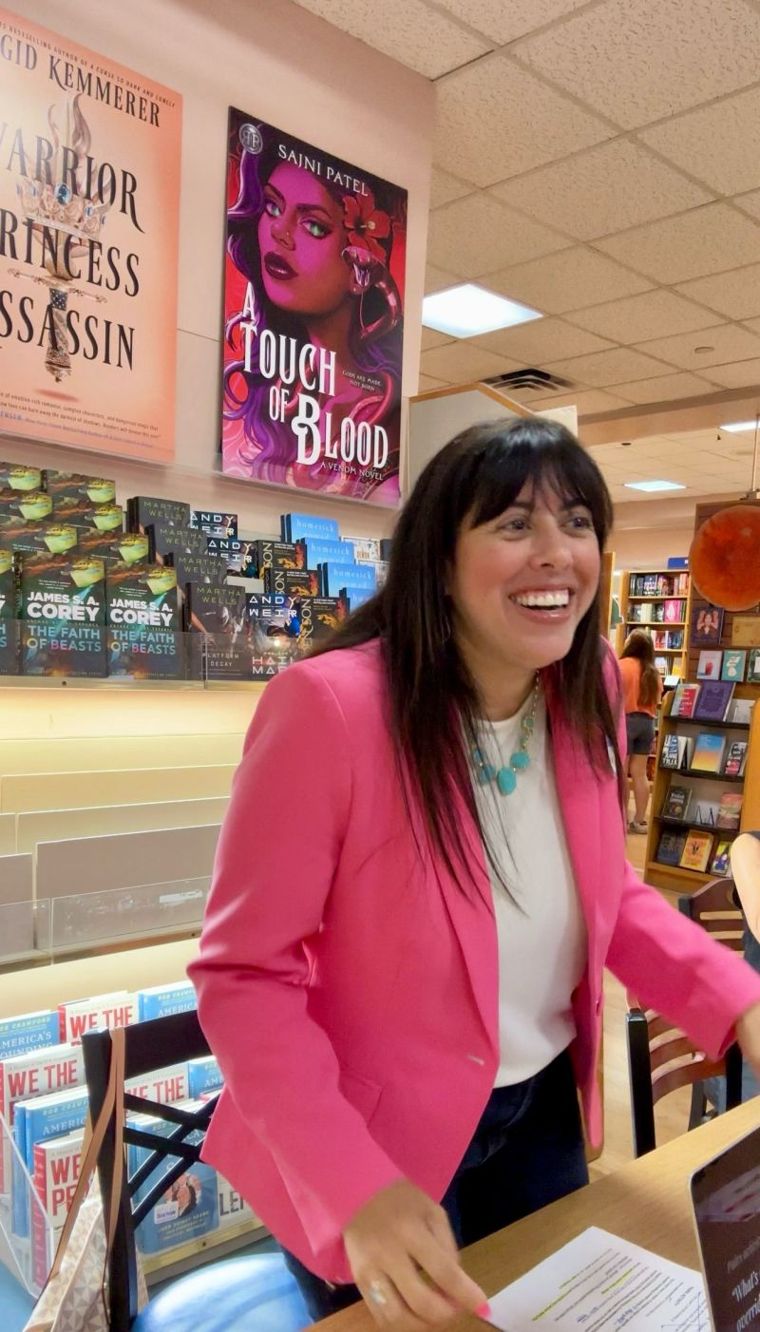 Holly Subervi laughing in a pink blazer while leading a session in a bookstore